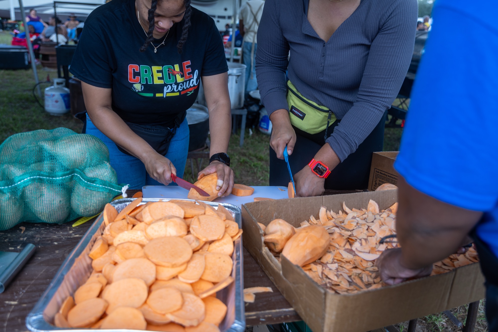 Slicing sweet potatoes into foil trays, a Creole Proud tee