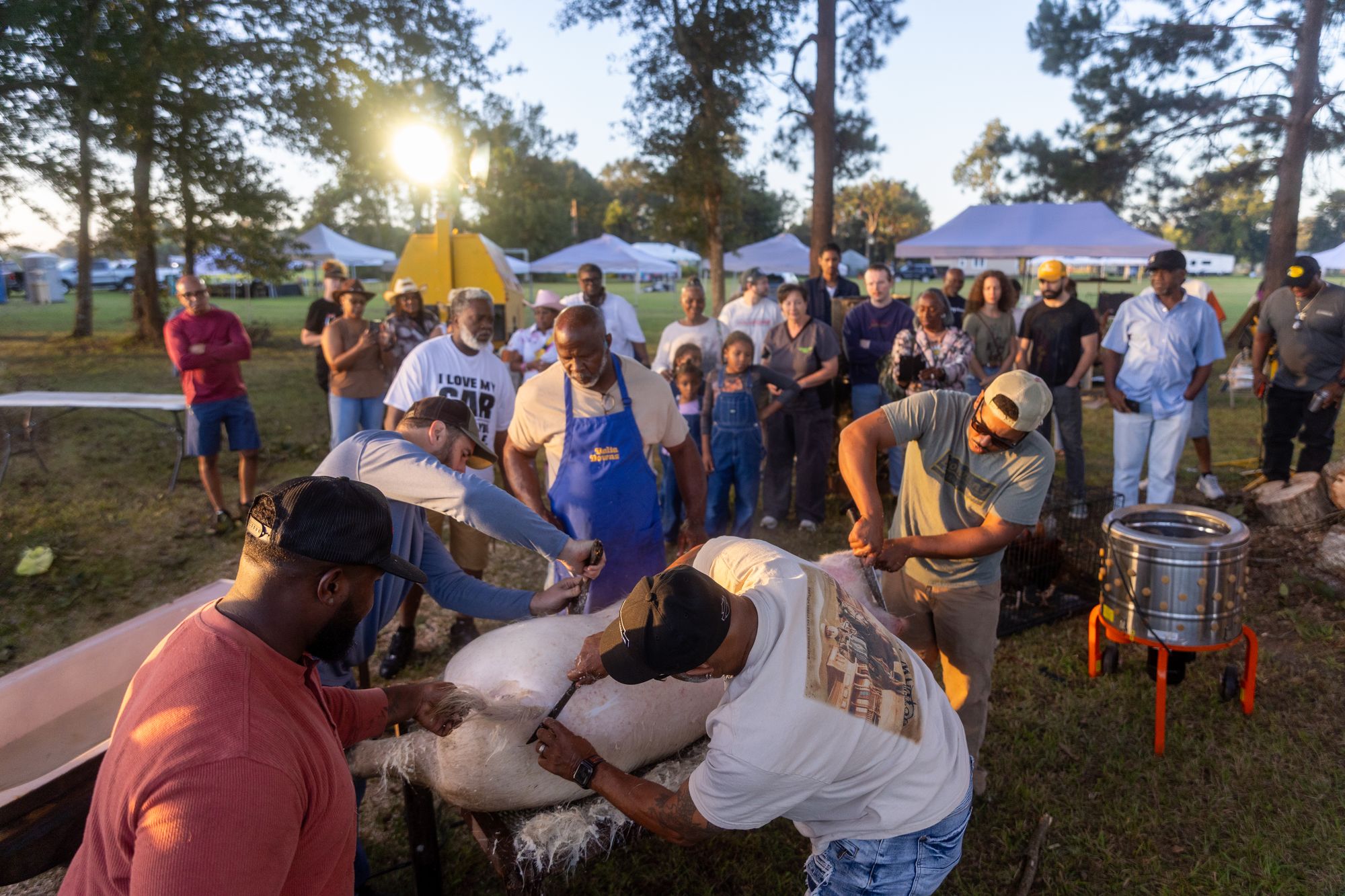 Community gathered around a live Creole boucherie at golden hour in Grand Coteau